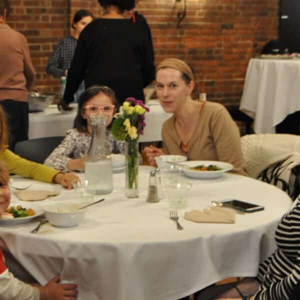 Two women and three children eat smile and eat dinner together at Cathedral Night at Saint John's Cathedral in Denver, CO.