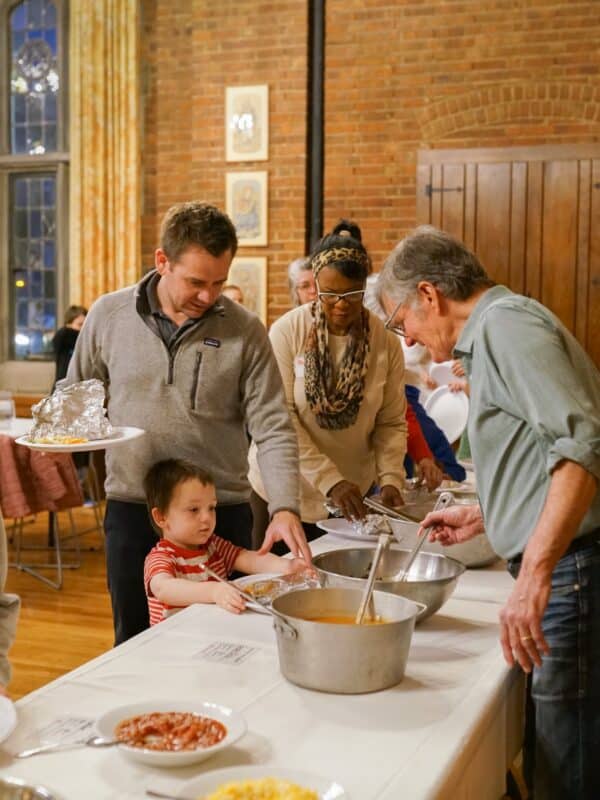 Adults and a young child serve food together during Cathedral Night at St. John’s Cathedral in Denver, sharing a community meal before worship and formation.