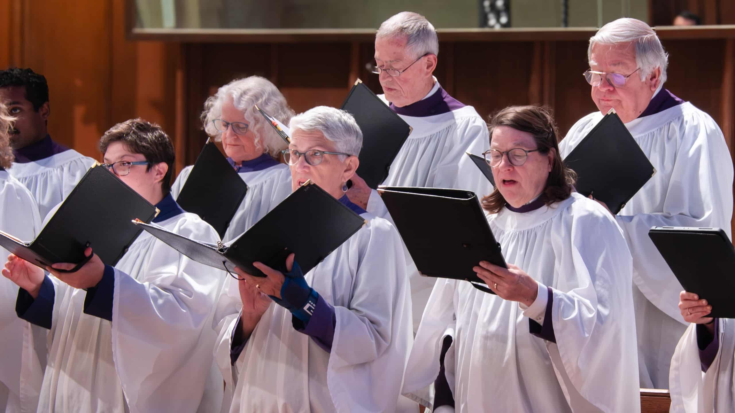 Members of the St. John’s Cathedral choir sing together in white robes during worship in Denver.