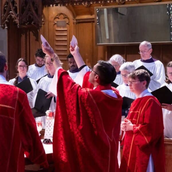 Clergy in red vestments raise their hands in prayer at the altar while the cathedral choir stands behind them.