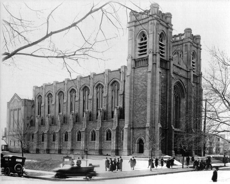 Historic black-and-white photograph of St. John’s Cathedral in Denver showing the Gothic Revival exterior, twin towers and people gathered along the street.