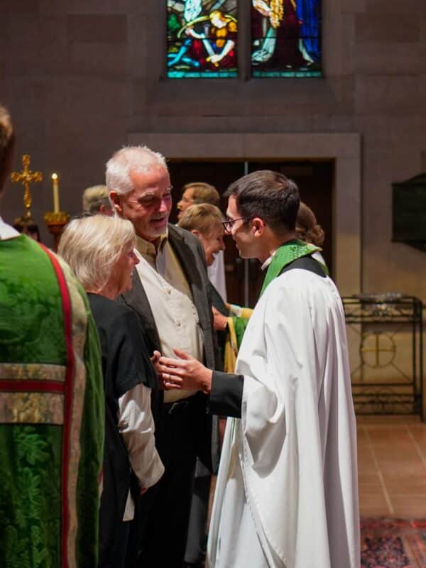 A member of the clergy speaks with two parishioners inside St. John’s Cathedral in Denver, reflecting the cathedral’s pastoral care, prayer and spiritual support ministries.