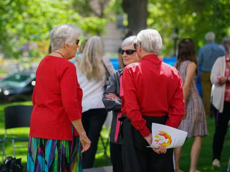 Three members of Saint John’s Cathedral visit outdoors during a Pentecost coffee hour, with one holding a worship bulletin.