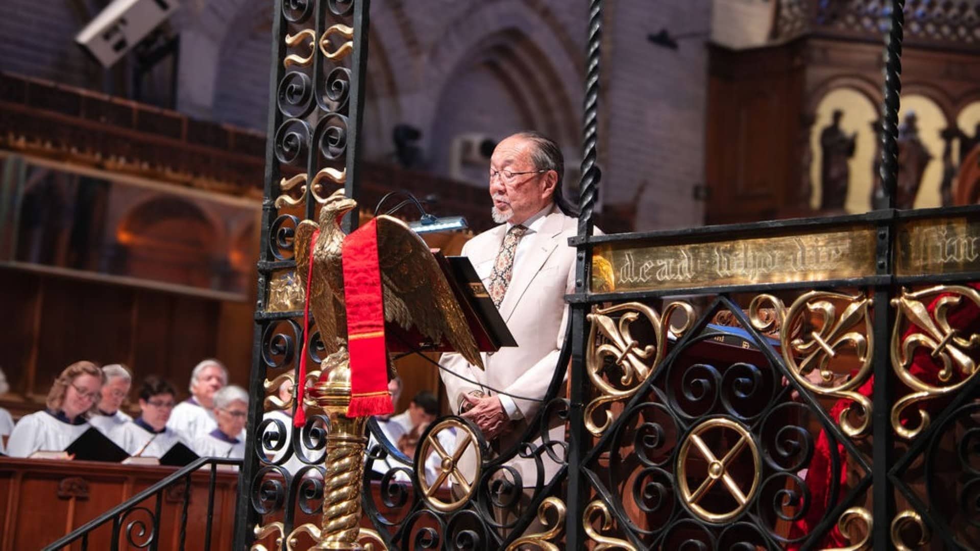 A reader speaks from the lectern at Saint John’s Cathedral with the choir seated nearby during worship.