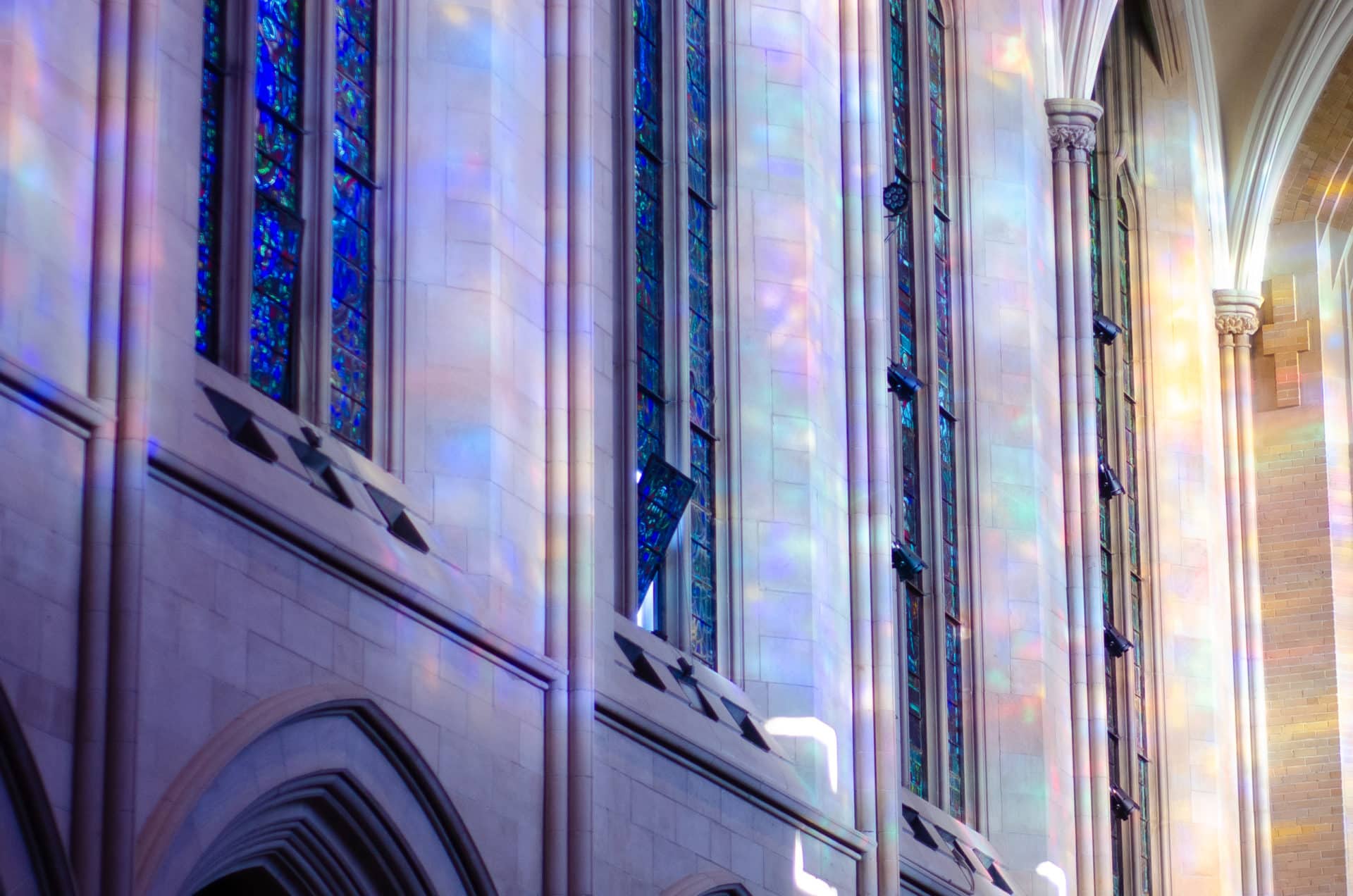 Colored light from stained glass windows illuminating the stone walls inside Saint John’s Cathedral.