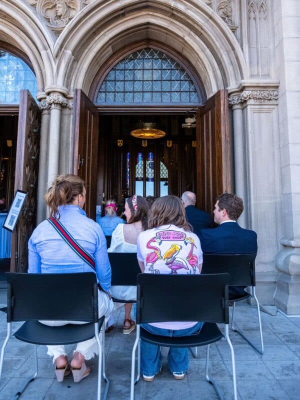 Visitors sit outside the open entrance of Saint John’s Cathedral, with the Cathedral’s Gothic stonework framing the doorway.