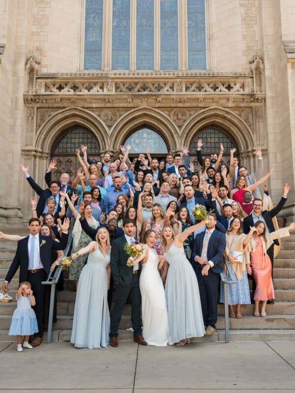 Large wedding party gathered on the front steps of St. John’s Cathedral in Denver, celebrating outside the cathedral entrance.